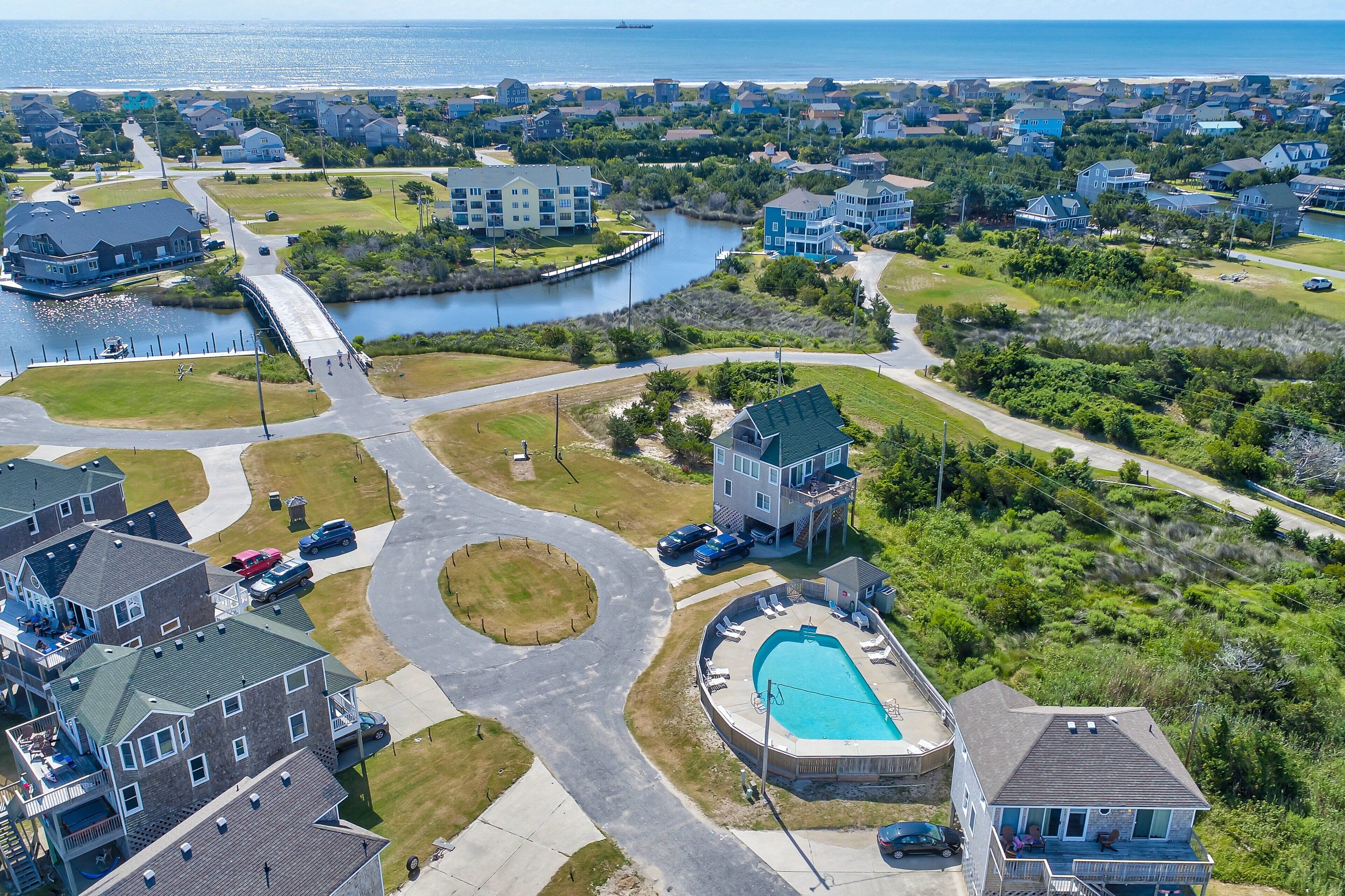 A residential area with a large swimming pool, a bridge over a water body, and houses with various architectural styles.
