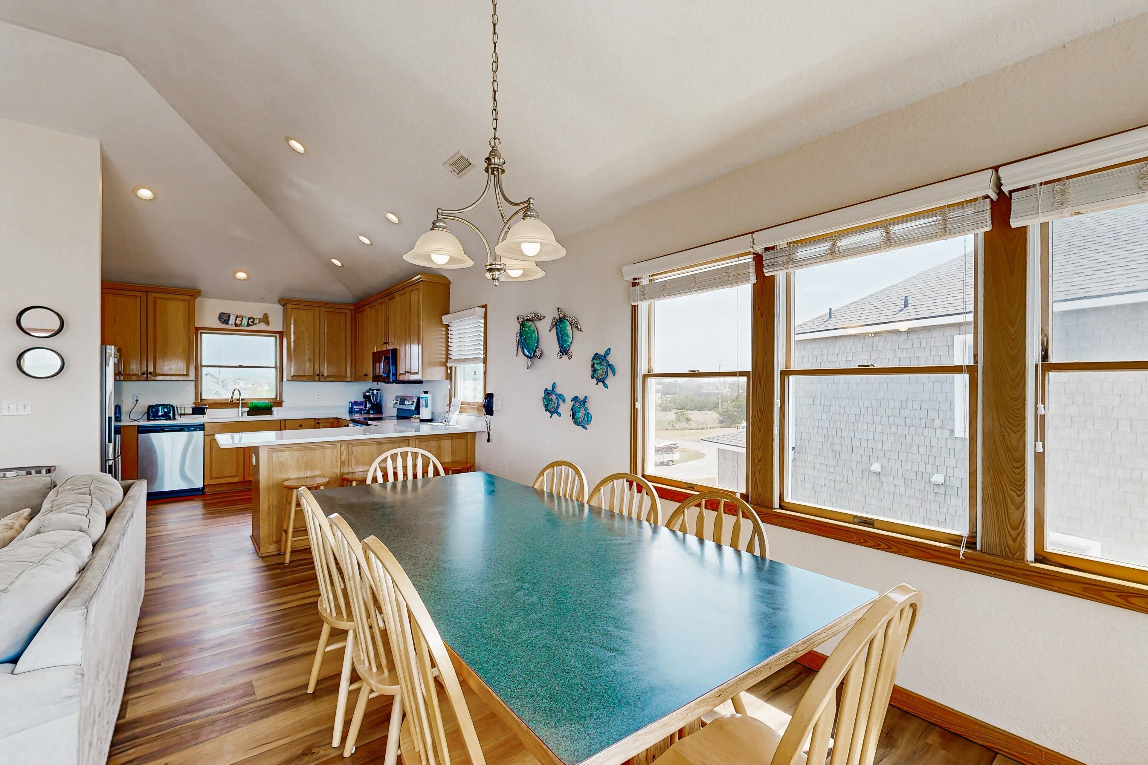Una cocina amplia con armarios de madera, una mesa de comedor con sillas y un gran ventanal con persianas.