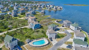 Vista aerea di una zona residenziale con case, una piscina e un pontile che si protende in uno specchio d'acqua.