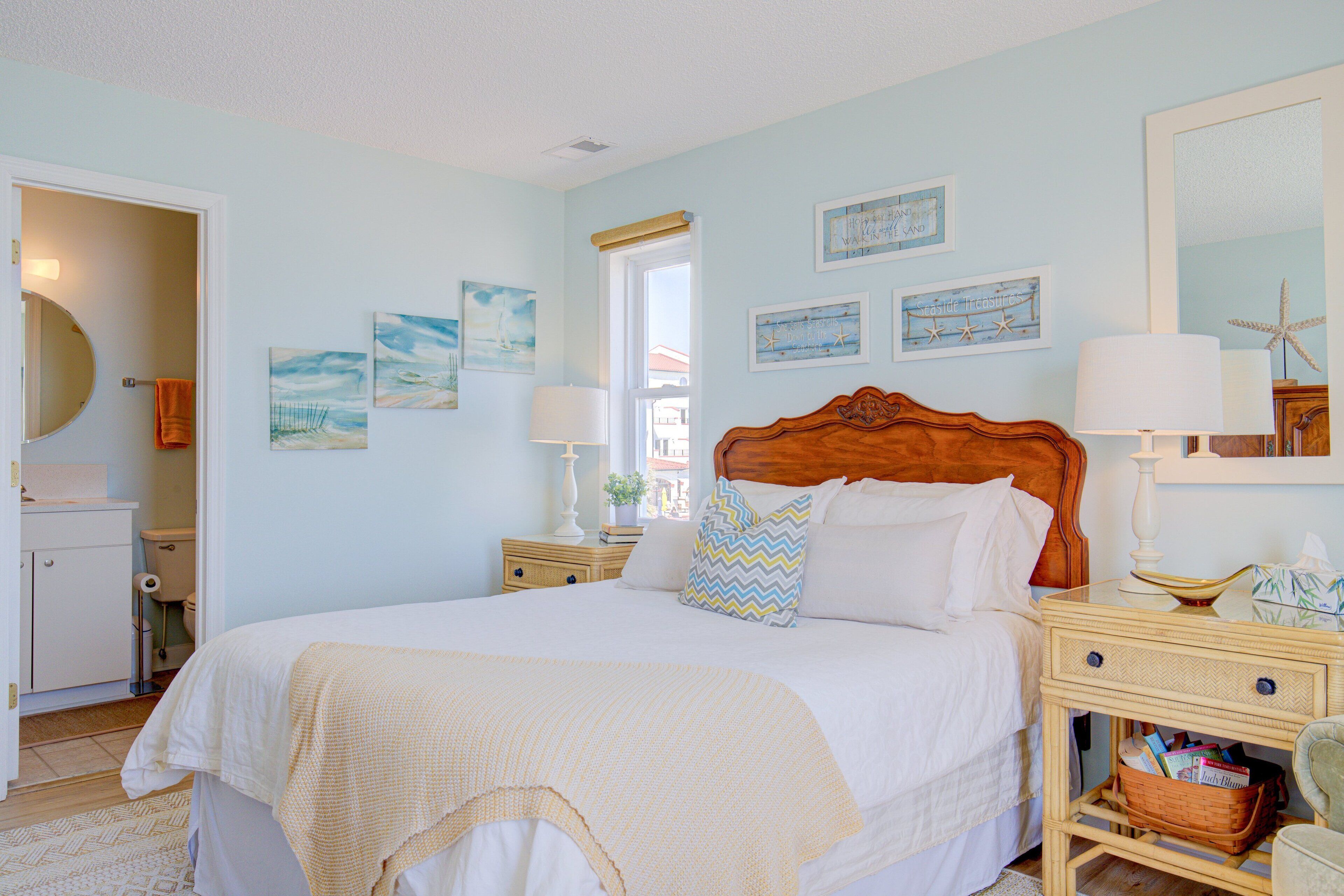 Une chambre à coucher comprenant un lit, des tables de chevet, une commode, une lampe, un miroir et des œuvres d’art murales.