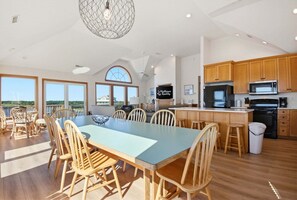 Un vaste espace dédié à la salle à manger, avec une longue table et des chaises, une cuisine dotée de meubles en bois et une grande fenêtre offrant une vue sur le paysage.