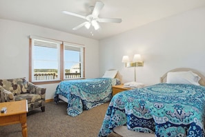 A hotel room with two beds, a ceiling fan, a sofa, a nightstand, and a lamp.