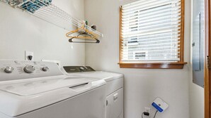 Een wasserette met een voorlader wasmachine en droger, een droogrek en een raam met jaloezieën.