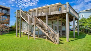 Un'area esterna con decking in legno e una scalinata che conduce a una zona coperta, circondata da un prato e da edifici vicini.