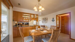Zona pranzo con tavolo in legno apparecchiato per quattro, circondato da sedie abbinate. Adiacente alla zona pranzo, una cucina con mobili in legno e forno a incasso.