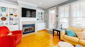 A living room with a fireplace, a red sofa, a beige sofa, and a TV mounted above the fireplace. - Beautiful beach house with an elevator, washer/dryer, & AC - walk to the beach (Wrightsville Beach)