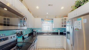 Une cuisine moderne avec des meubles blancs, un réfrigérateur en acier inoxydable et une cuisinière noire.
