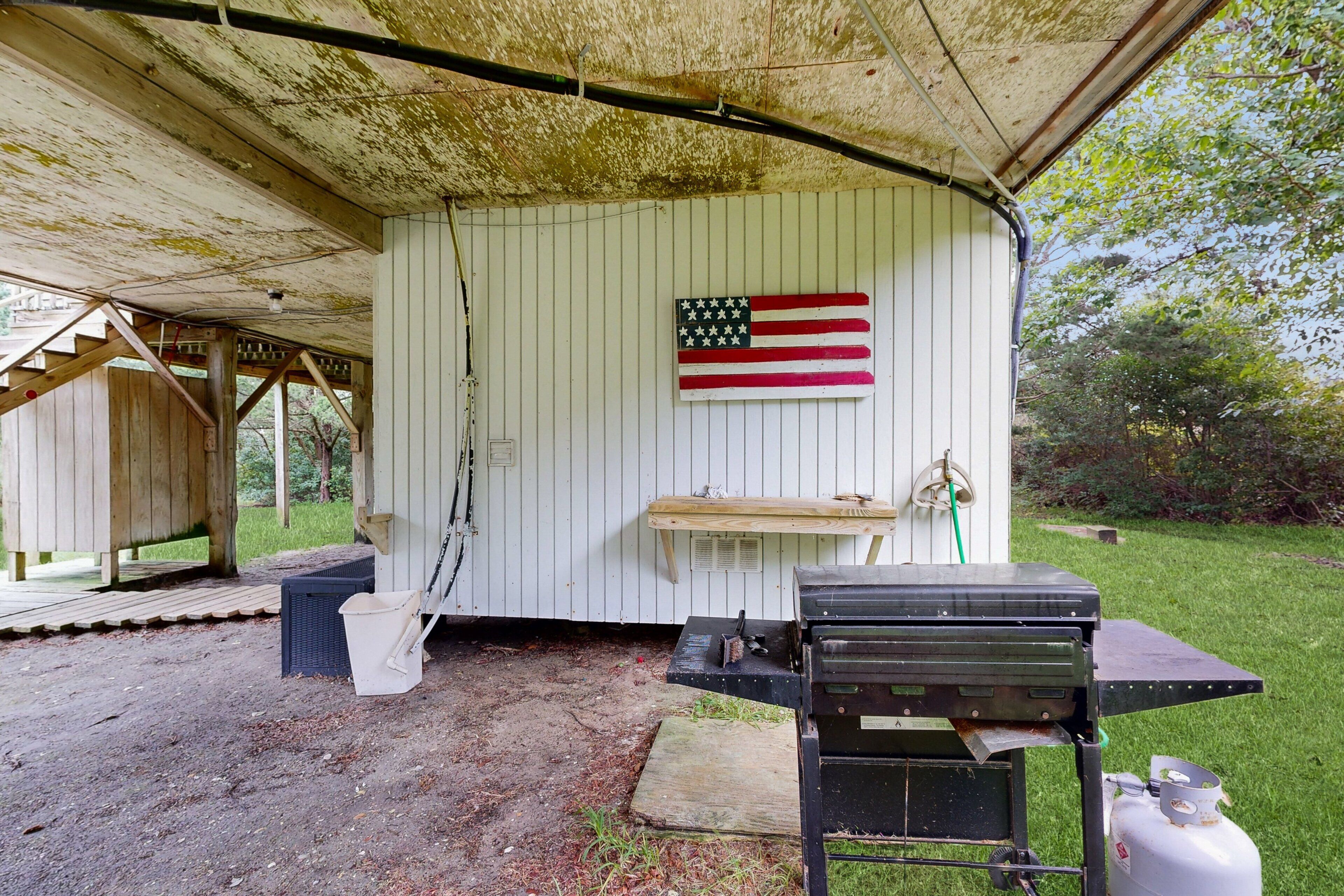A rustic outdoor kitchen area with a grill, a gas tank, and a wooden bench.