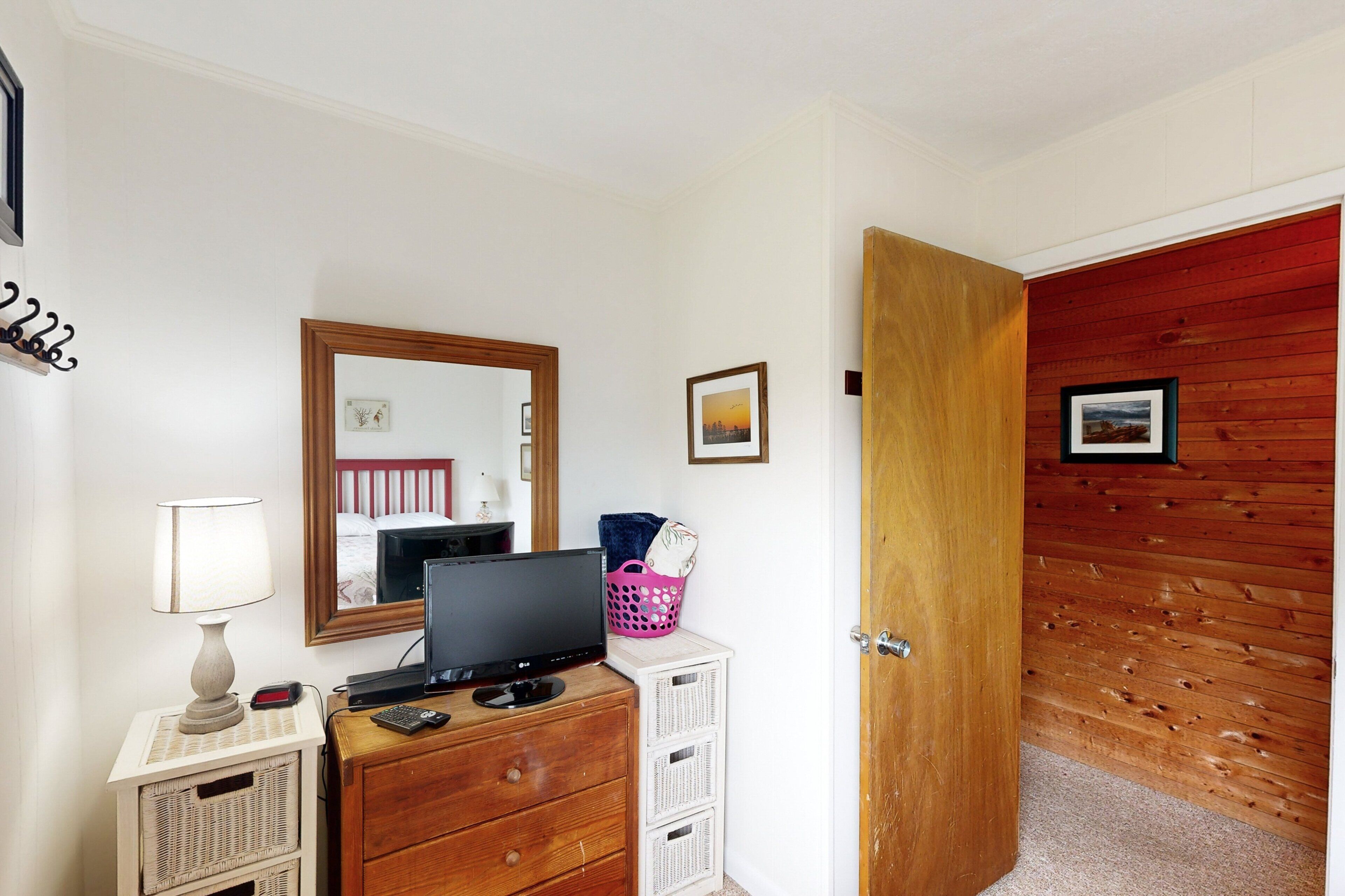 Une chambre avec une porte en bois, une commode sur laquelle se trouve un téléviseur, une lampe et un miroir.