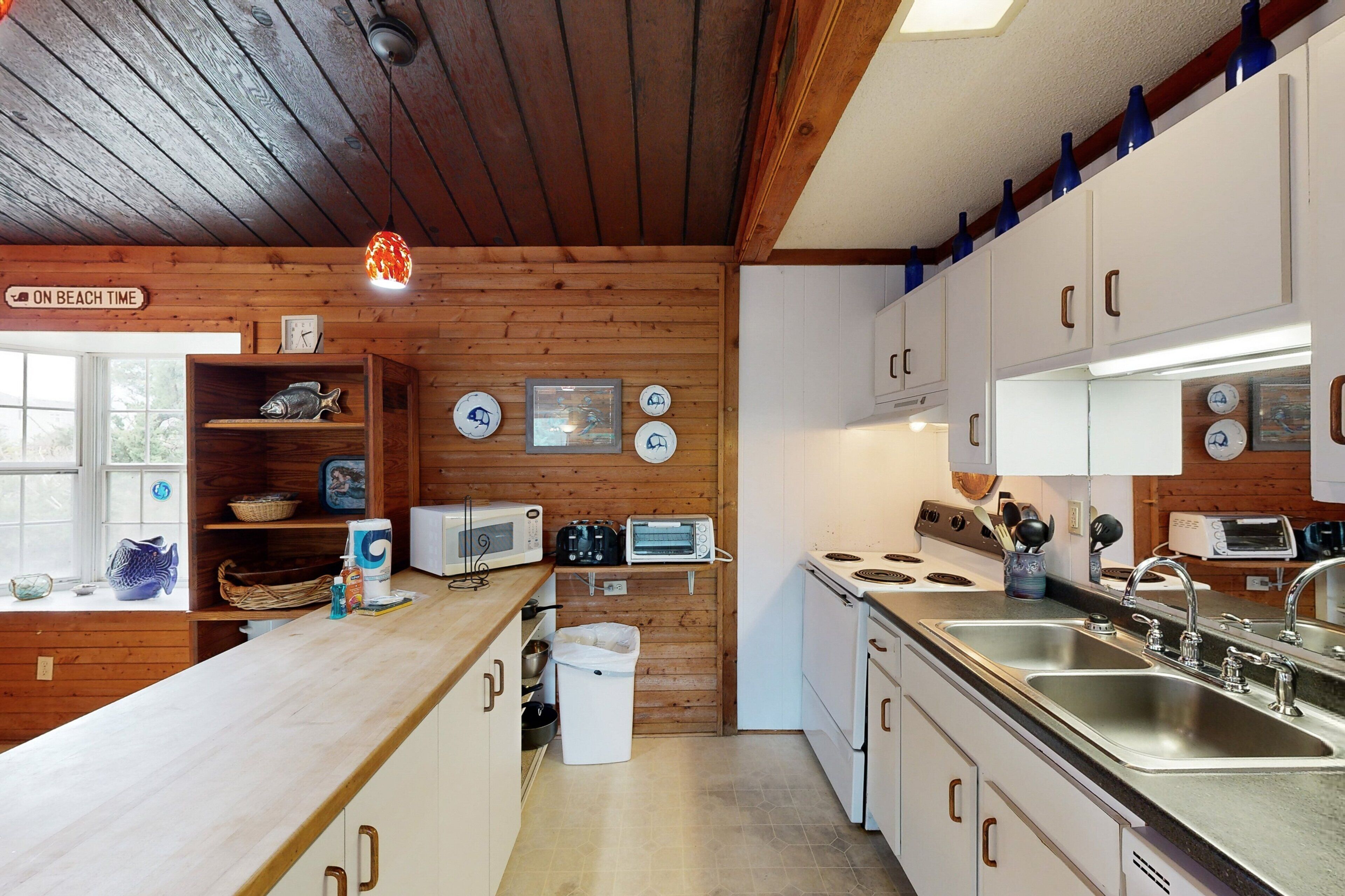 A kitchen with wooden walls, white cabinets, a double sink, and a stove.