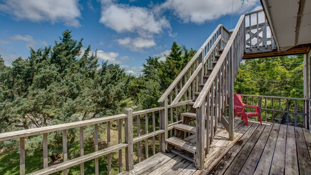 Um deck de madeira com escadas que levam a um espaço coberto, cercado por árvores.