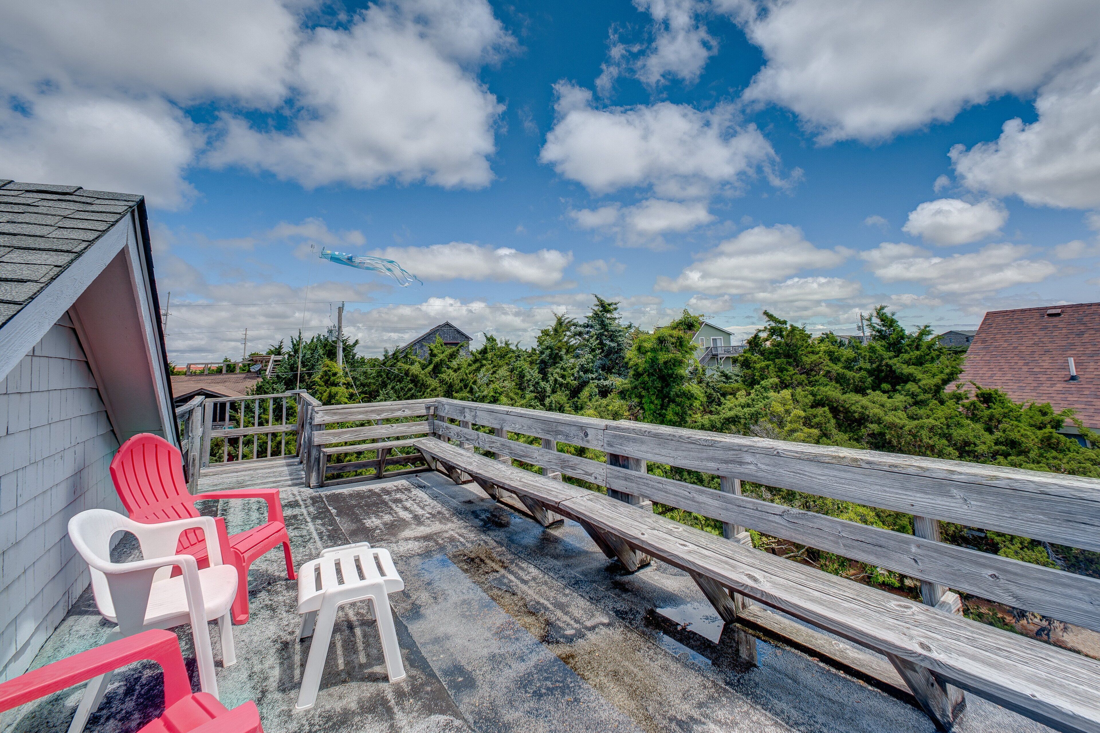 A wooden deck with picnic tables and chairs, overlooking a residential area with houses and trees.