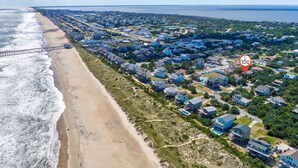 Vista aérea de uma área residencial costeira com casas, uma praia e um cais.