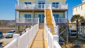 A two-story beachfront house with a wooden deck and a staircase leading to the upper level. - Beachfront home with beach access, elevator, ocean views, outdoor shower, W/D (North Topsail Beach)
