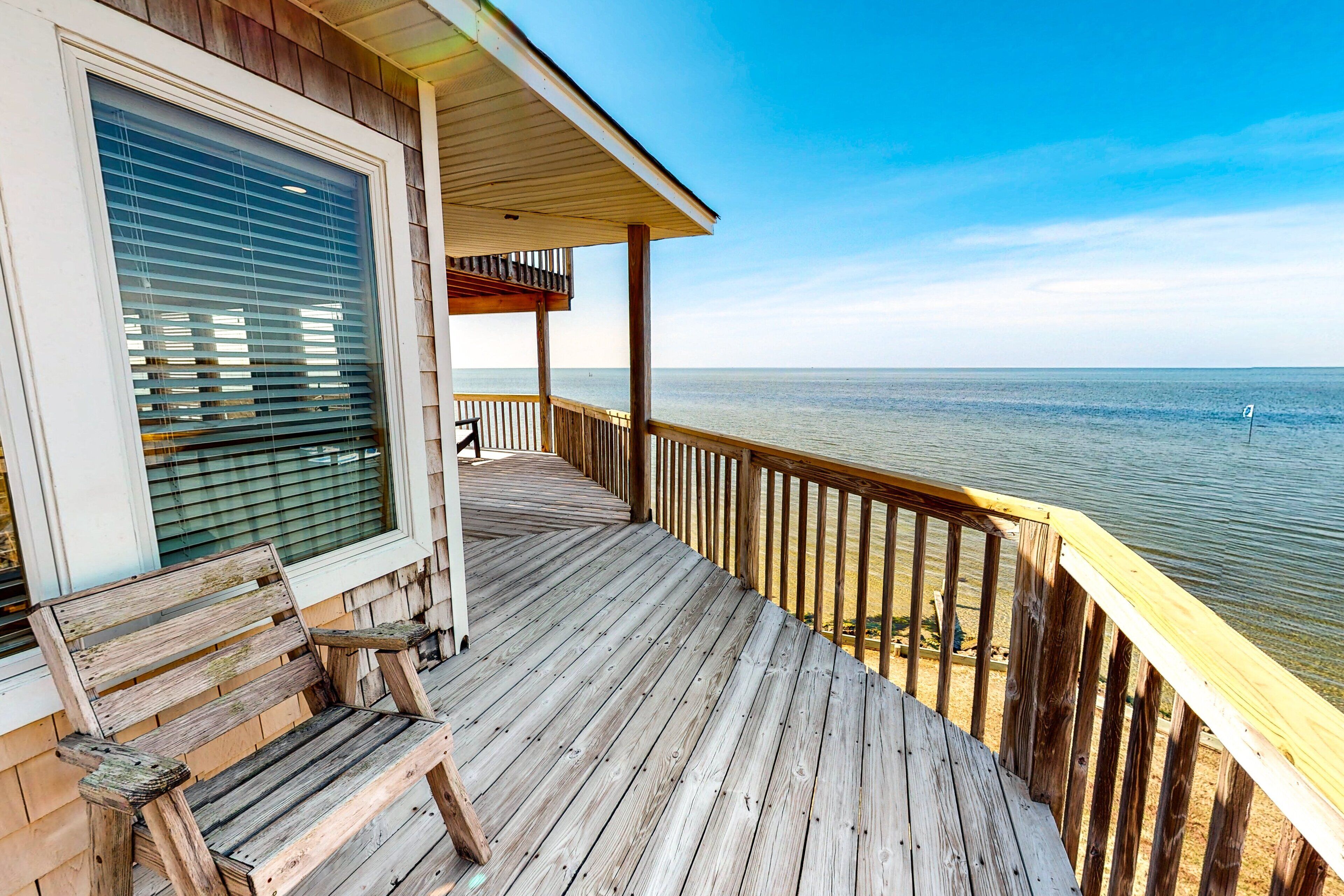 A wooden deck with a bench, overlooking a calm body of water.