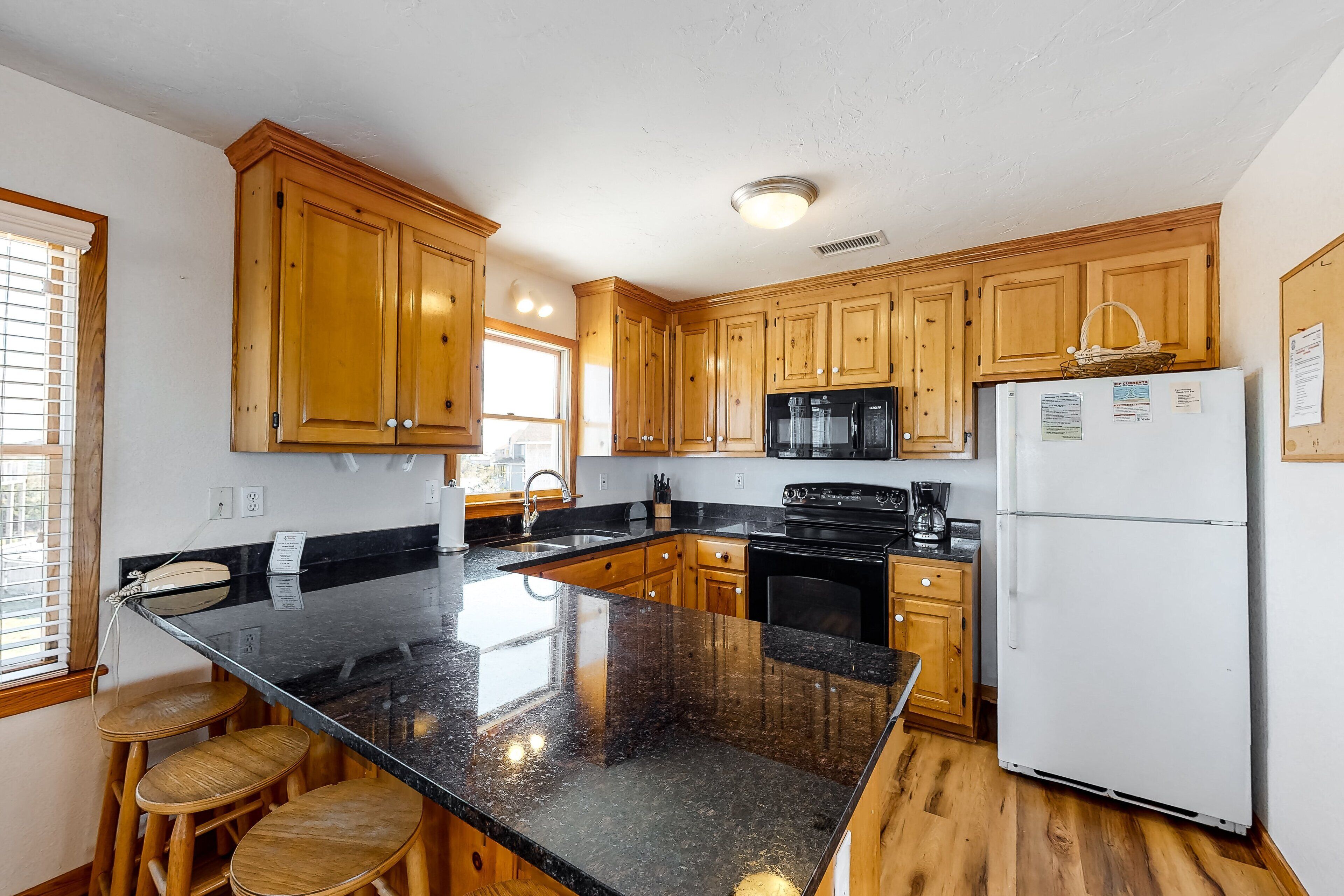 A kitchen with wooden cabinets, a black granite countertop, a refrigerator, and a sink.
