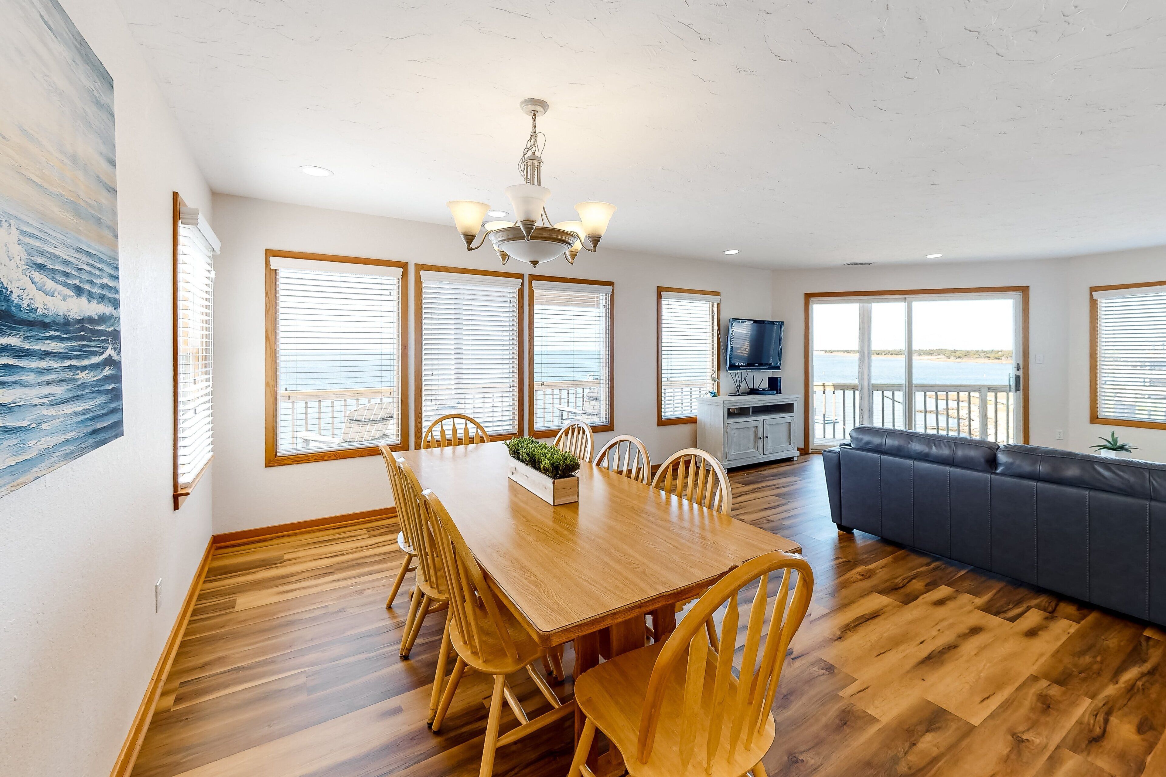 Un salon spacieux avec une table à manger en bois, un canapé foncé et de grandes fenêtres donnant sur la mer.
