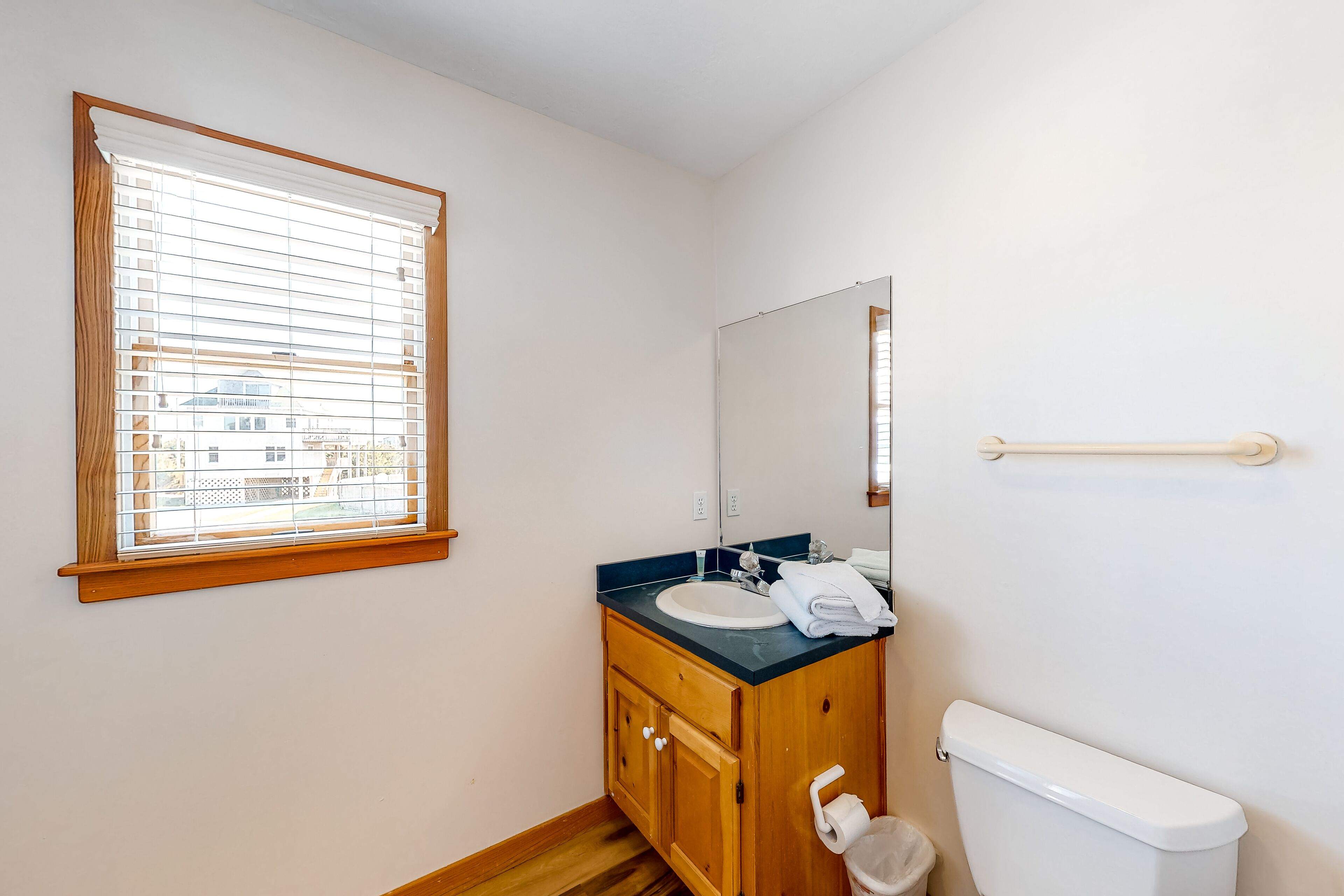 A bathroom with a wooden vanity, a white sink, a mirror, and a window with blinds.