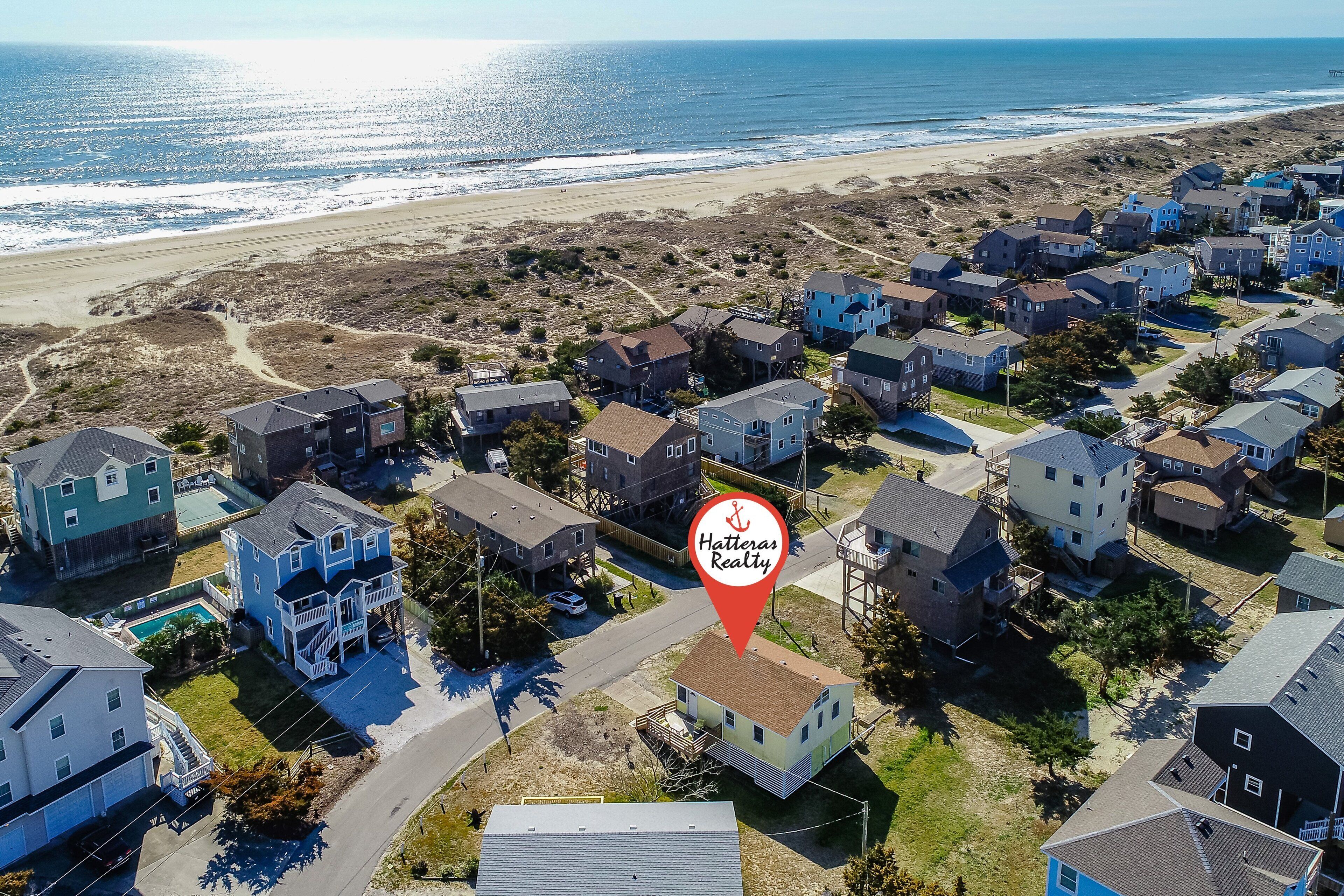 An aerial view of a coastal residential area with houses, a beach, and a marina.