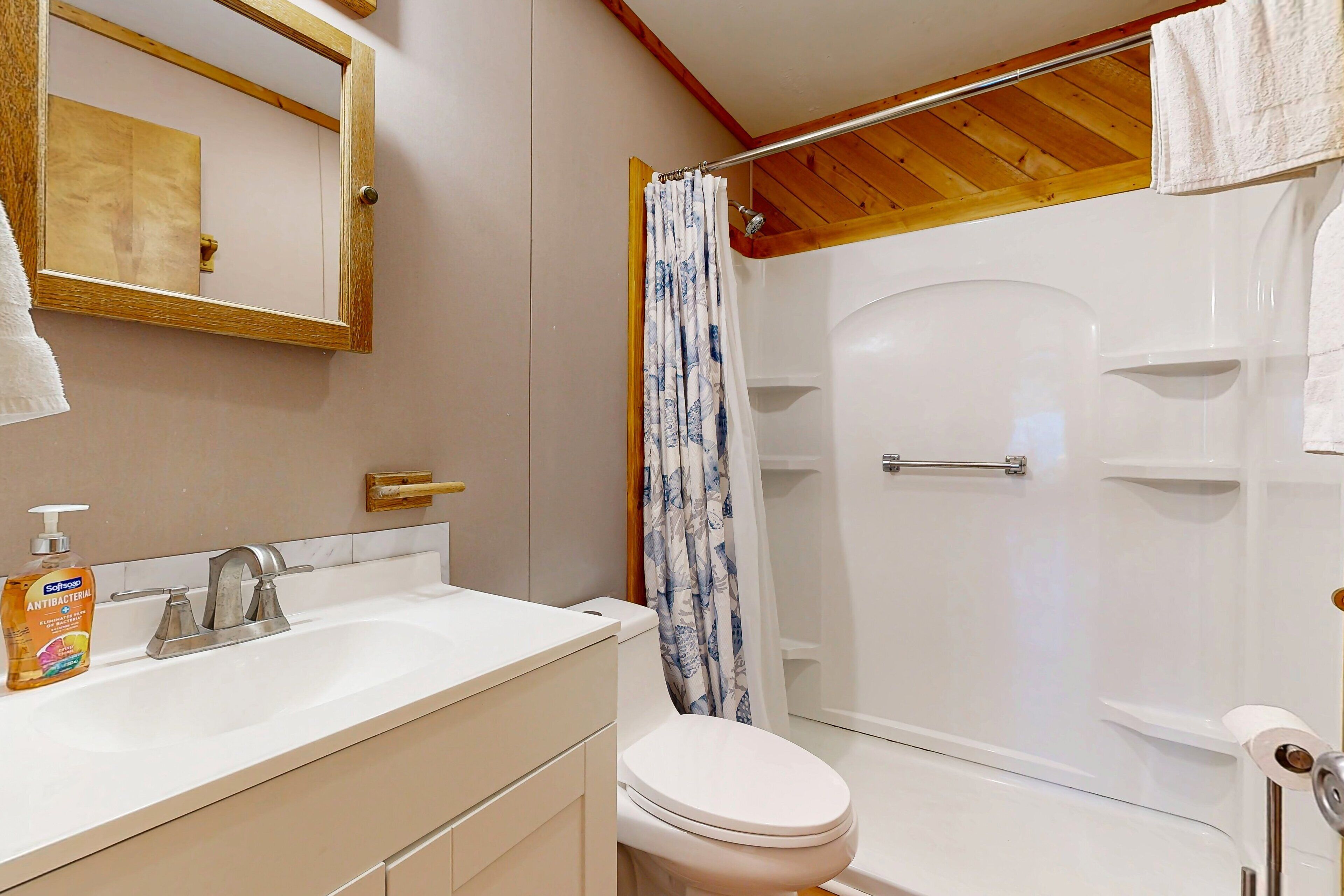 A bathroom with a white sink, a toilet, a shower with a blue shower curtain, and a wooden ceiling.