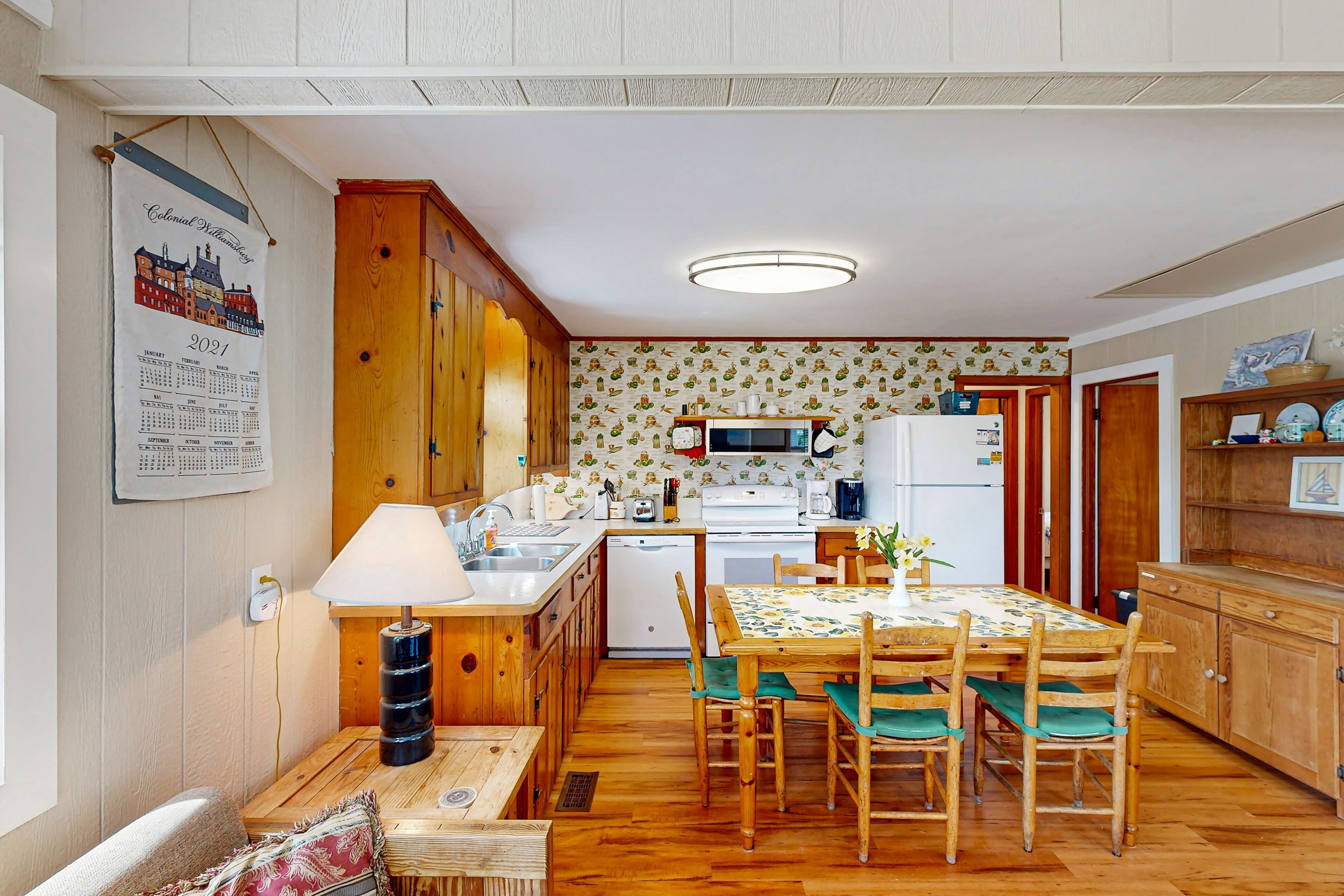 Uma cozinha compacta com armários de madeira, uma mesa de jantar com cadeiras, uma geladeira e um micro-ondas.