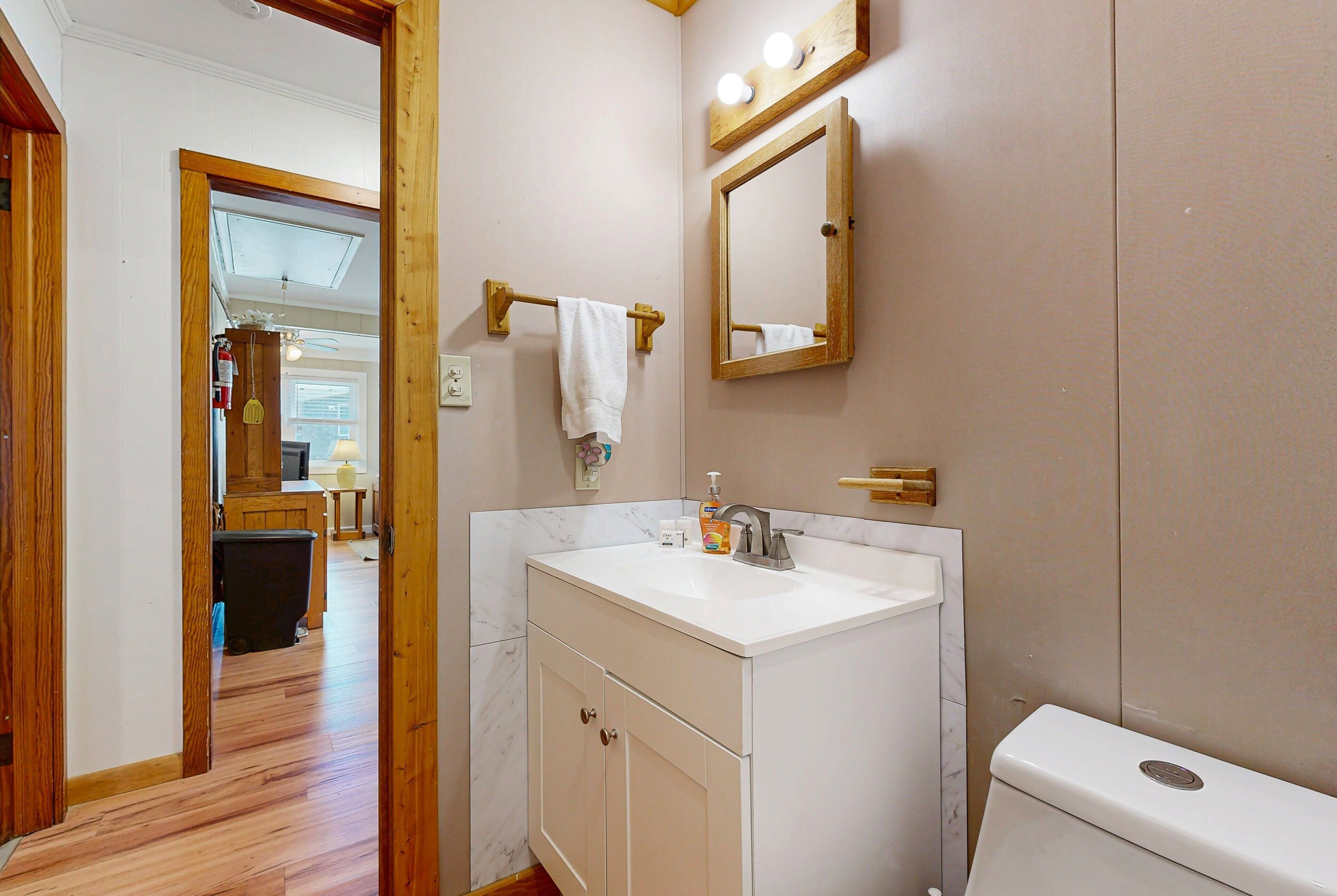 A bathroom with a white sink, a mirror, and a toilet. There is a towel hanging on a towel rack.
