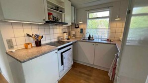Kompakti keittiö, jossa on valkoiset kaapit, sisäänrakennettu uuni ja ikkuna, josta tulee luonnonvaloa.