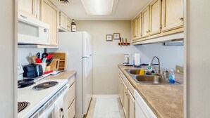Une cuisine de taille réduite, avec des appareils électroménagers blancs, des meubles en bois et un évier.