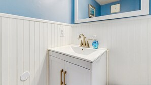 Une salle de bain avec un lavabo blanc, un robinet doré et un miroir au-dessus.