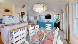 Una cocina moderna con barra, taburetes blancos, una mesa de comedor con sillas rosas y un candelabro.