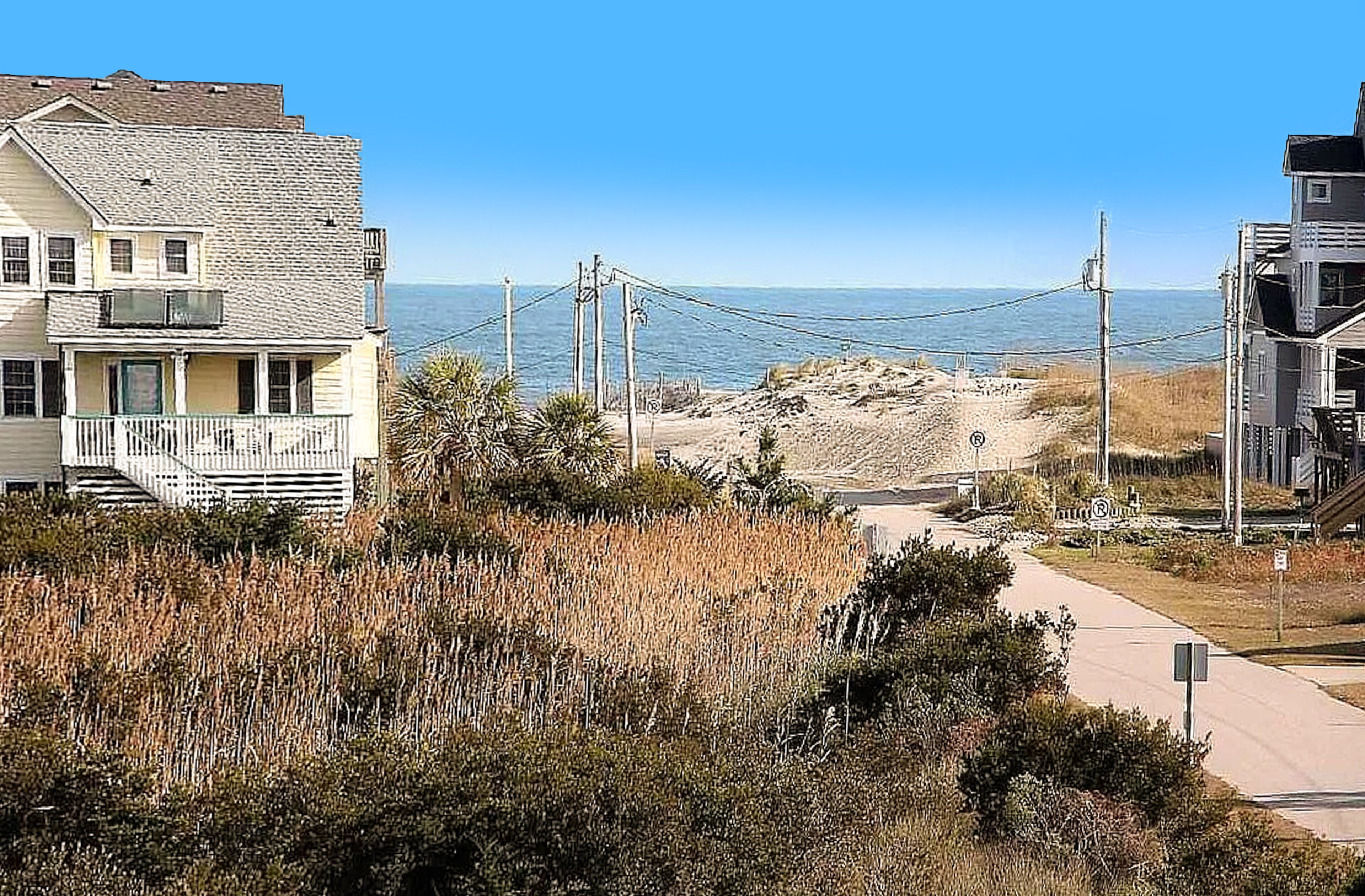 A coastal house with a front porch, a pathway leading to the beach, and a view of the ocean.