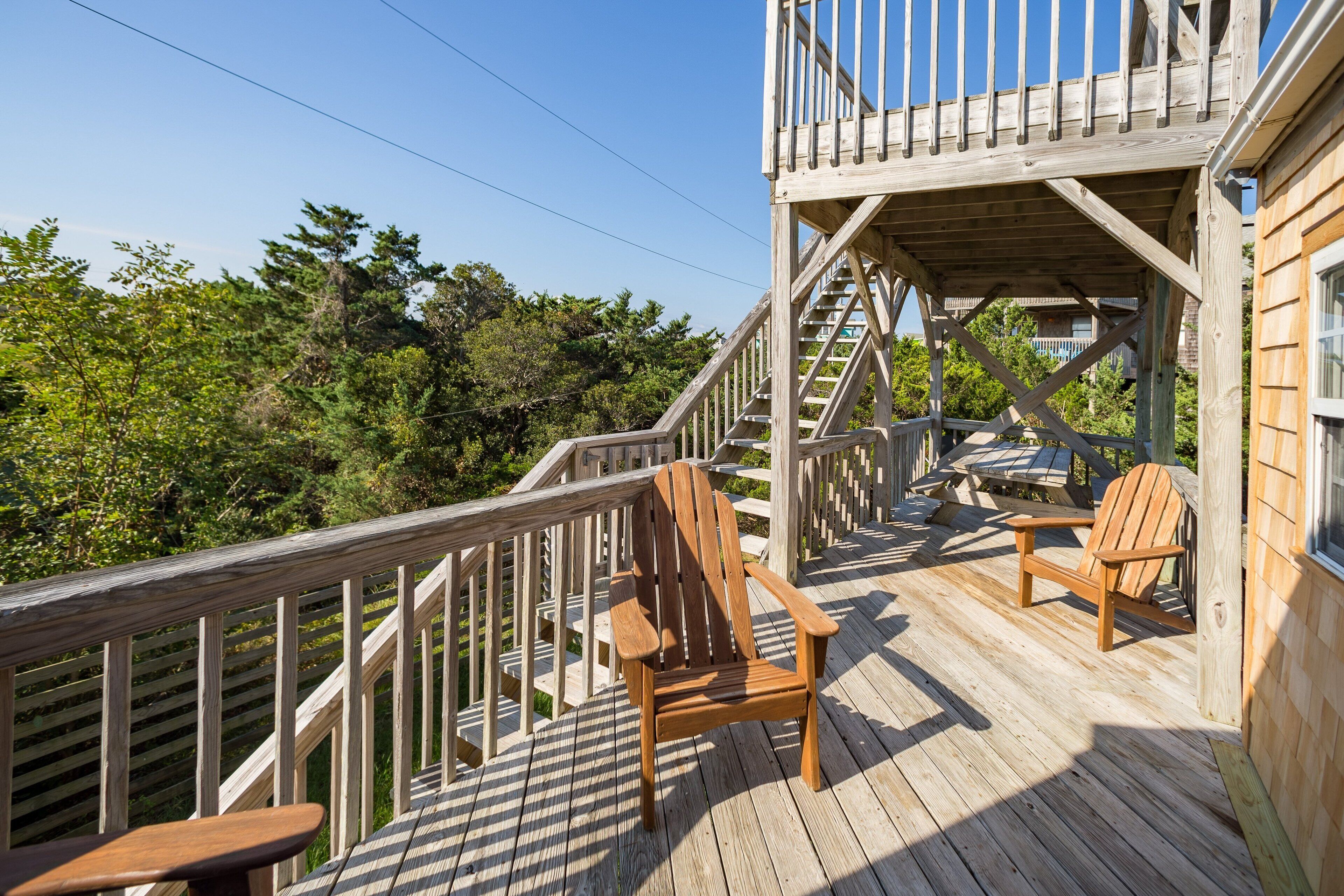 Una terraza de madera con una silla y una mesa de madera, una escalera de madera y vistas a árboles.
