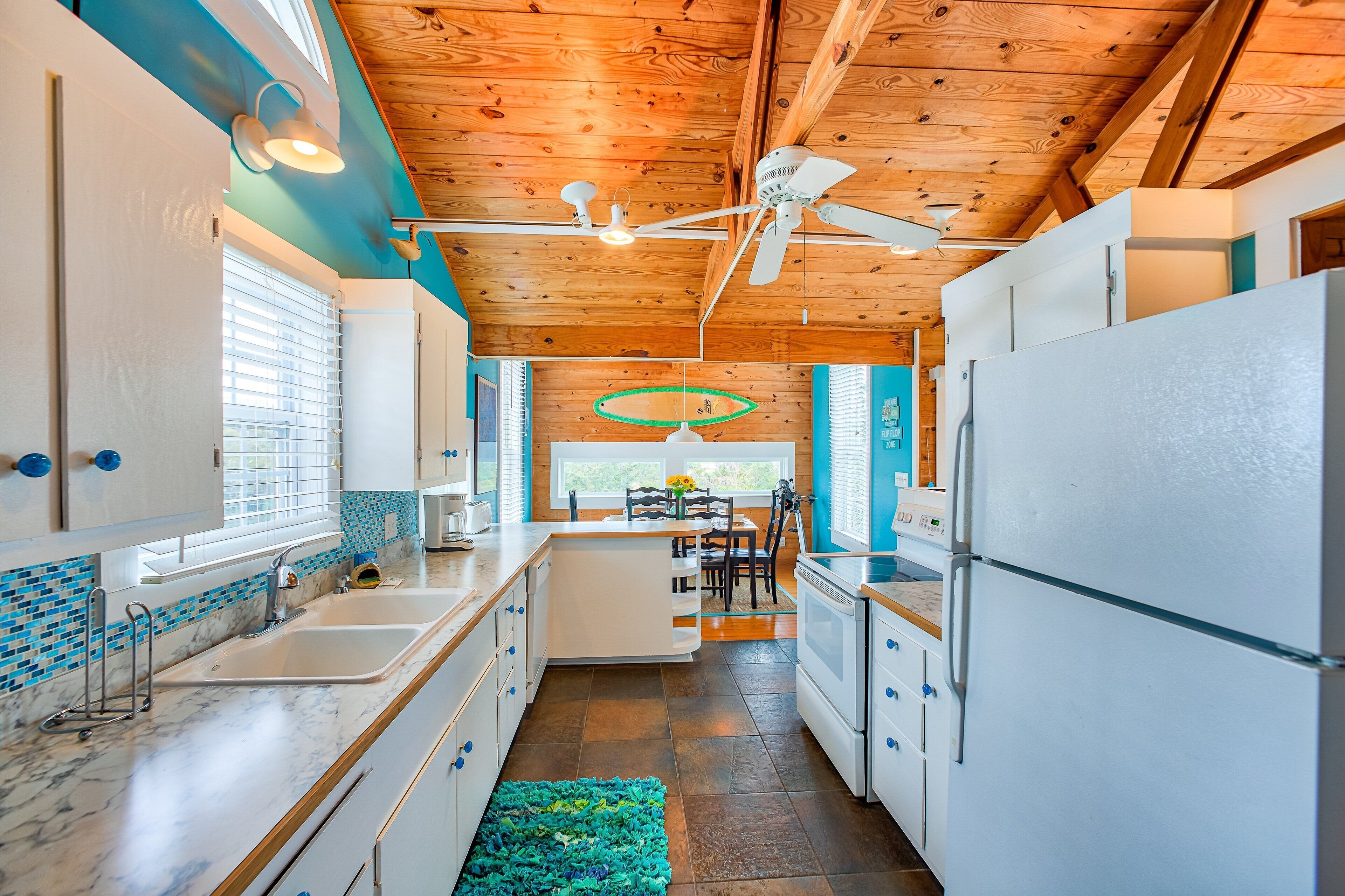 A modern kitchen with white appliances, a wooden ceiling, and a blue accent wall.