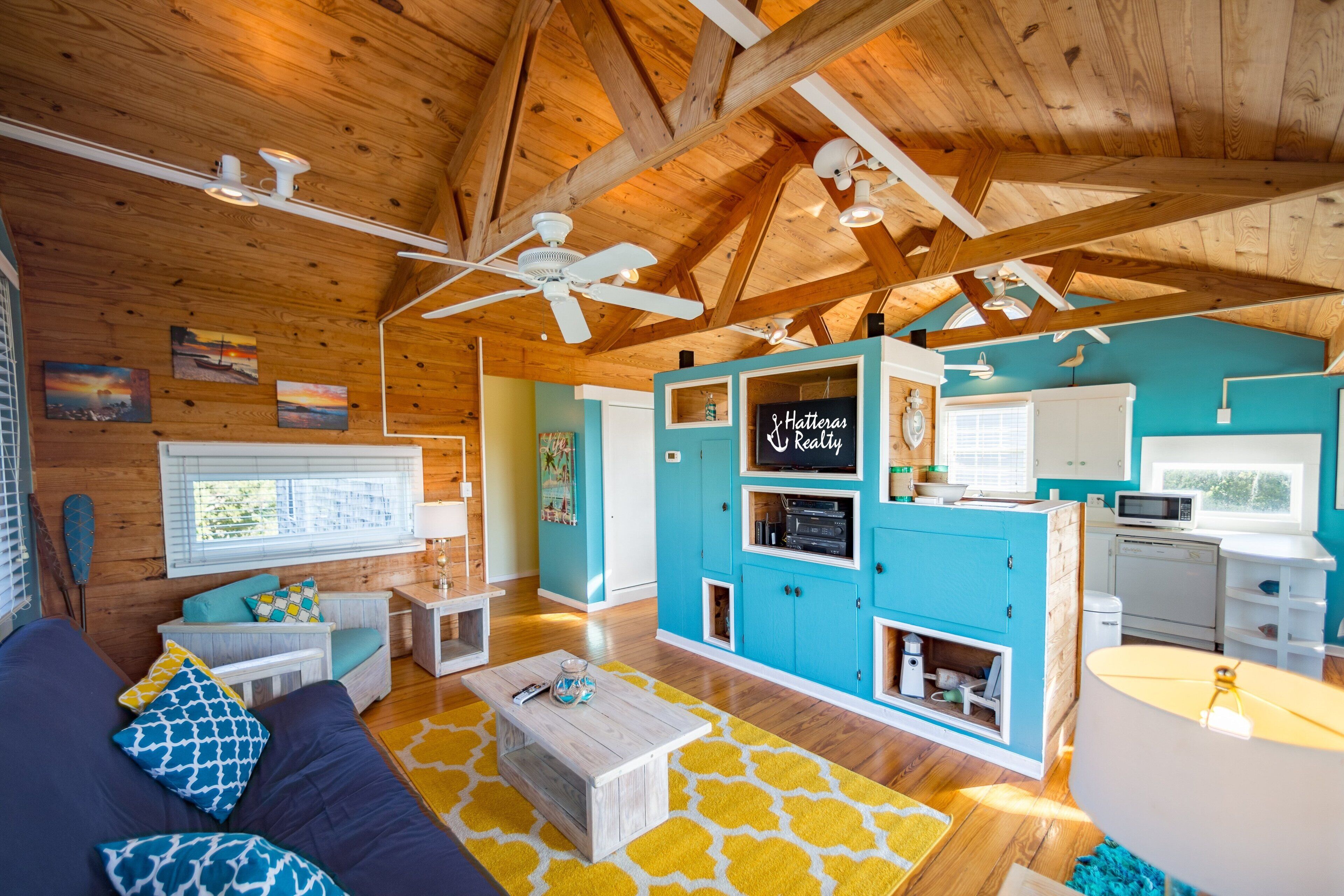 A spacious living room with a high ceiling, wooden beams, a blue accent wall, and a cozy seating area with a sofa and coffee table.