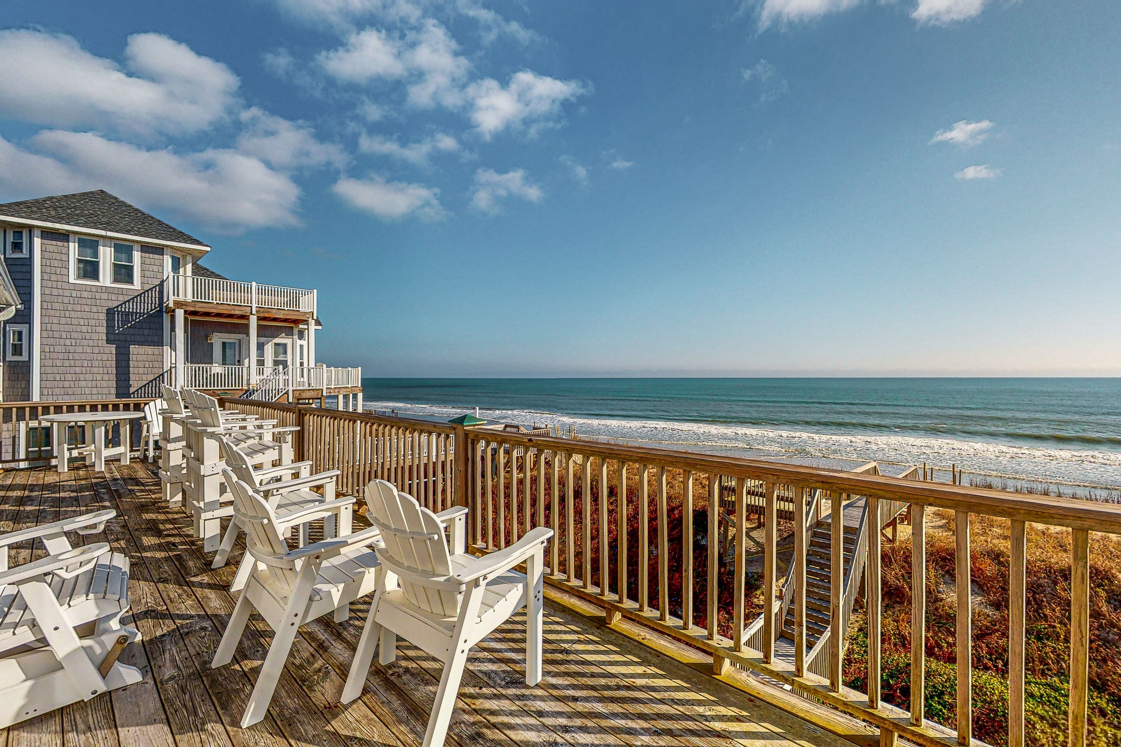 A wooden deck with white chairs overlooking a beach.