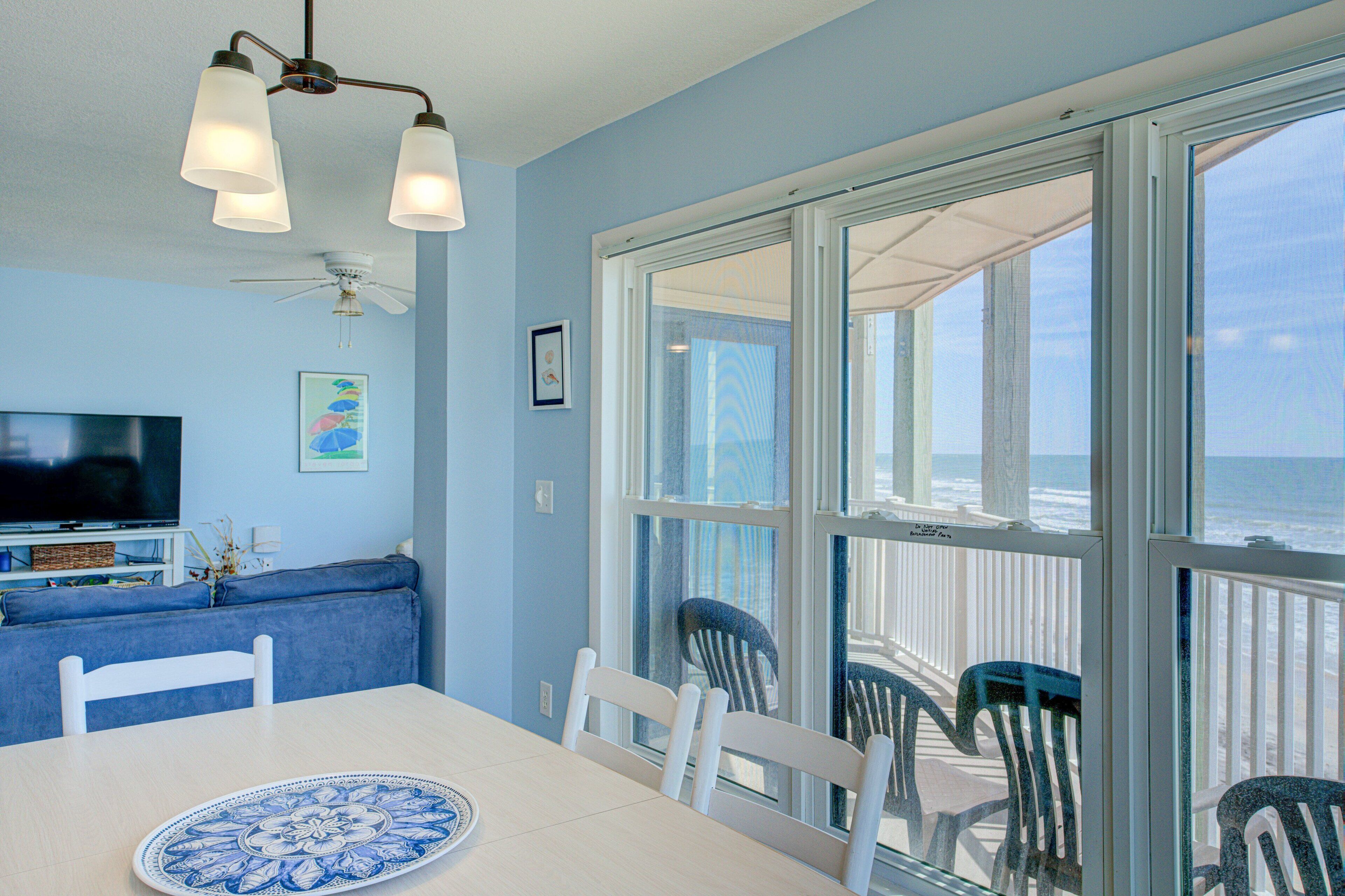 A dining area with a table, chairs, and a view of the ocean through large windows.