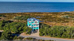 A large, two-story house with a balcony, surrounded by dense greenery and a view of the ocean. - Sound front home with amazing views, private pool, hot tub, theater & rec room (Avon)