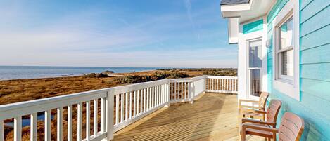 A wooden deck with white railings overlooking a beach.