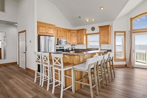 A kitchen with wooden cabinets, a stainless steel refrigerator, a microwave, and a large island with bar stools. - Sound front home with amazing views, private pool, hot tub, theater & rec room (Avon)