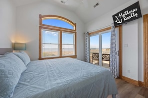 Une chambre avec un grand lit, un téléviseur fixé au mur et un balcon avec vue.