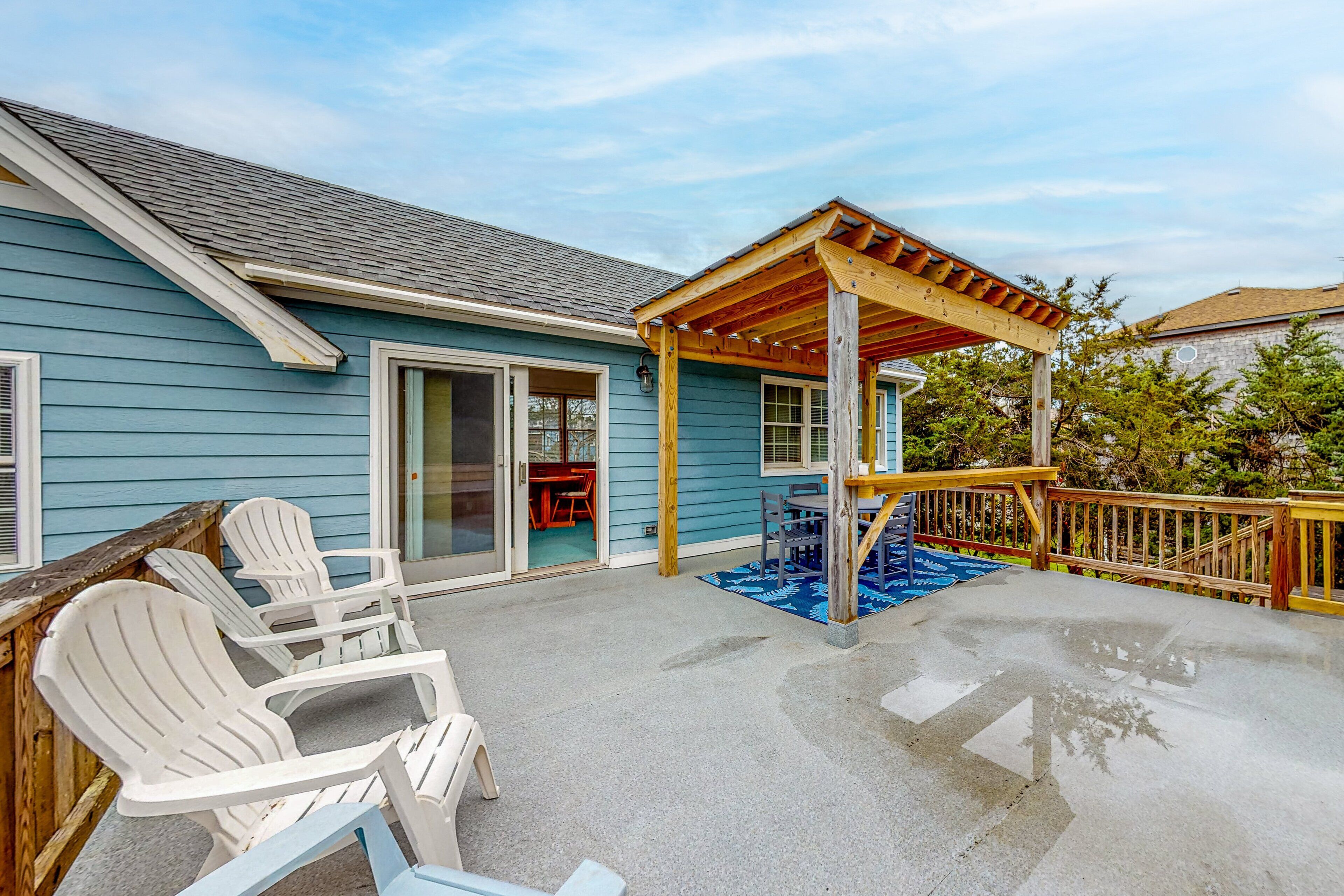 A covered patio with Adirondack chairs, a wooden deck, and a pergola.