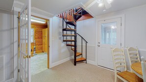 A room with a wooden staircase, a door, and a dining area with chairs and a table.