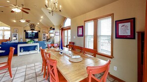 A spacious dining area with a wooden table and orange chairs, a blue sofa, and a chandelier. - 3-story luxury home with pool, hot tub, AC, tennis, & deck - dog-friendly (Avon)