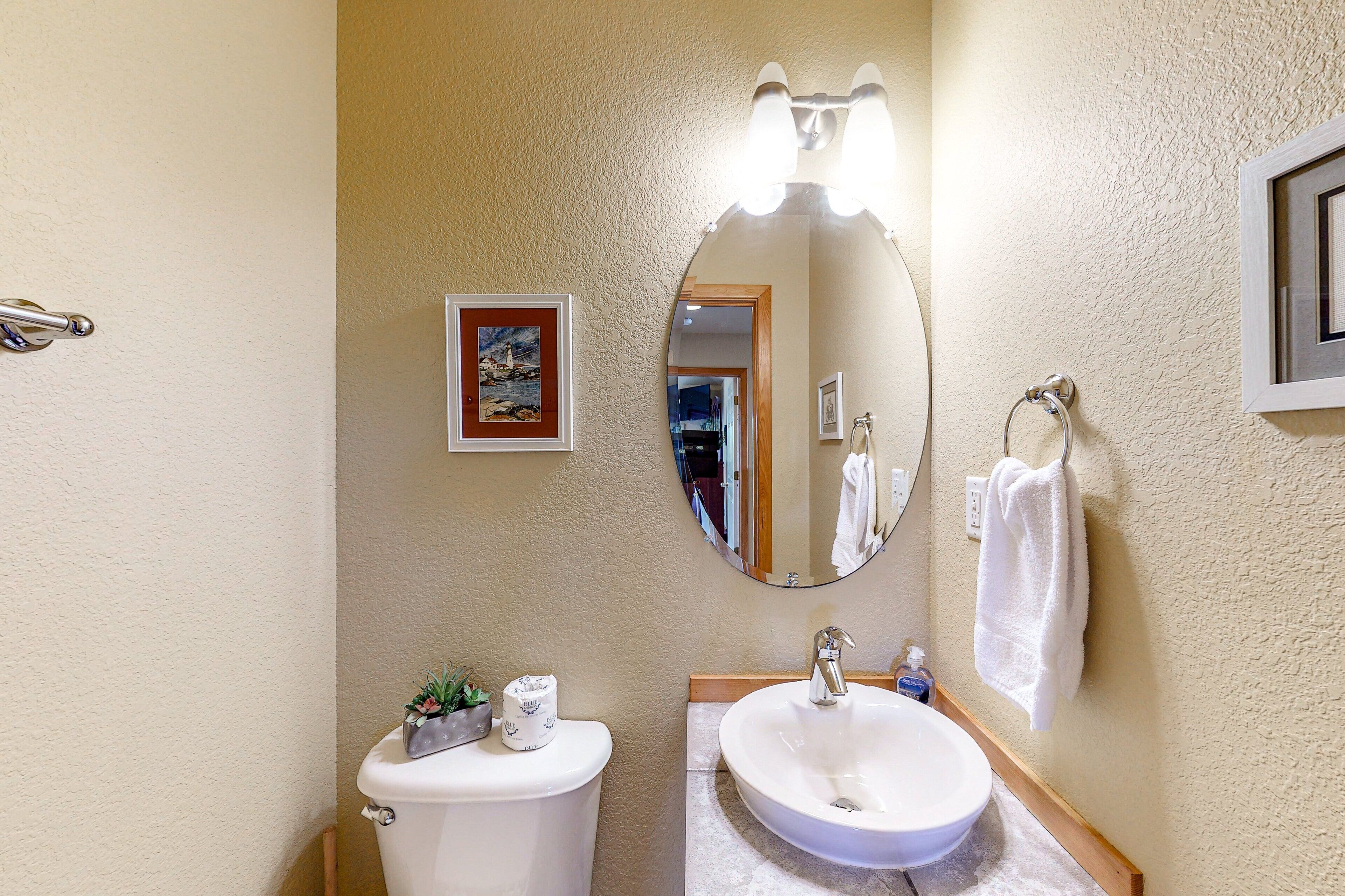 Un bagno con il water, un lavandino e uno specchio. C'è un portasciugamani con un asciugamano appeso, e un quadro incorniciato al muro.