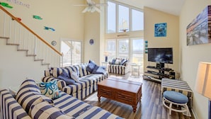 A spacious living room with striped sofas, a wooden coffee table, a TV, and a staircase. - Spacious, dog-friendly home with ocean views, beach access, & pool (North Topsail Beach)