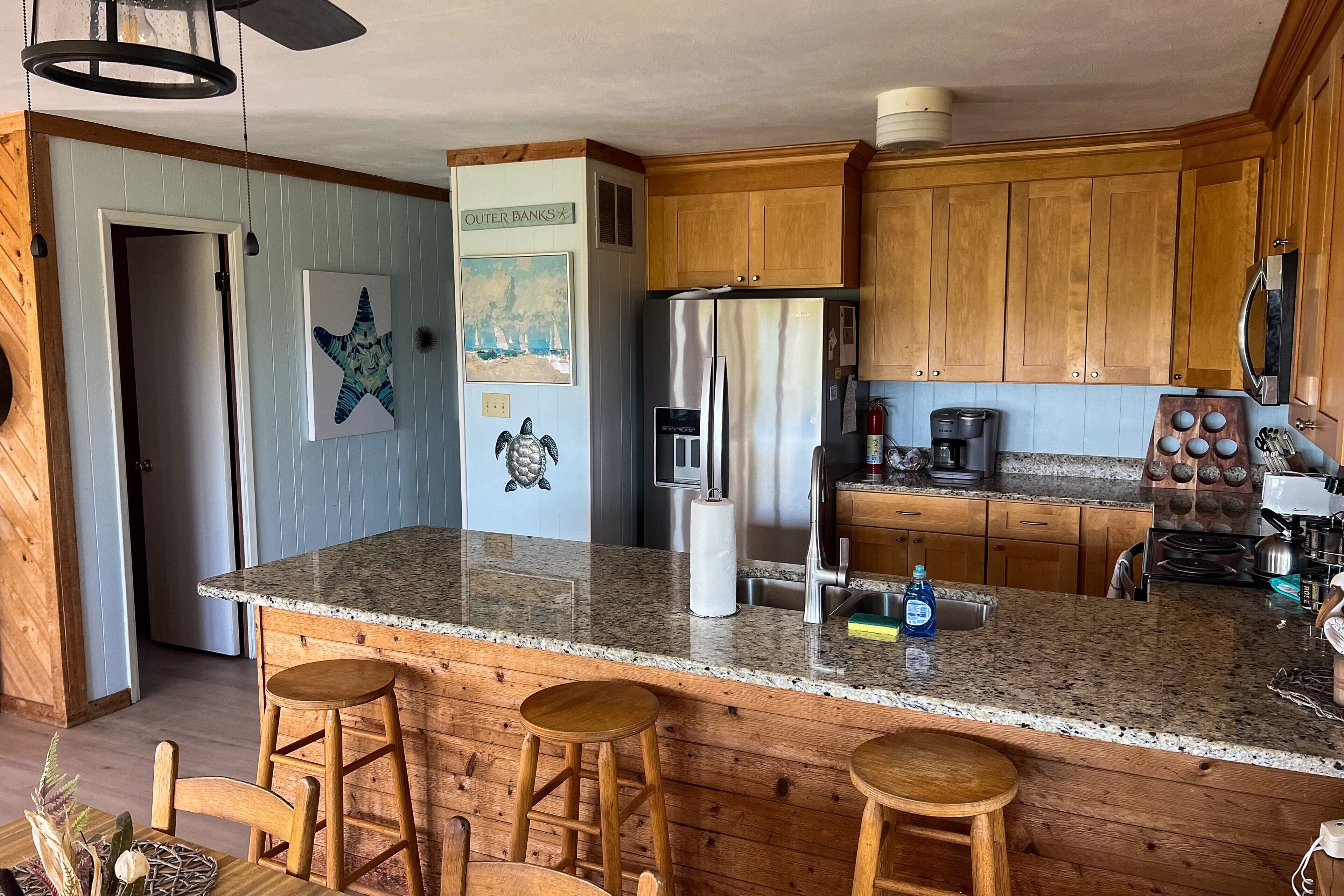 Una cocina con gabinetes de madera, encimera de granito, refrigerador de acero inoxidable y cafetera.