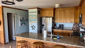 Una cocina con armarios de madera, un refrigerador de acero inoxidable, encimeras de granito y una zona de bar con taburetes.