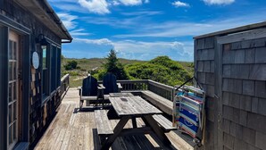 Una terraza de madera con mesas y sillas de picnic, con vistas a un paisaje pintoresco.