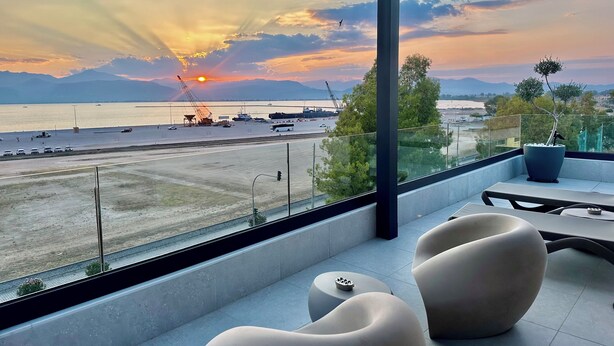 Ein moderner Balkon mit Blick auf einen Sonnenuntergang über dem Wasser, ausgestattet mit zeitgemäßer Möbel und einem Blumentopf.