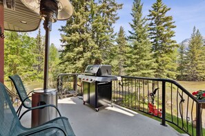 Une terrasse extérieure équipée d’un barbecue, de chaises et offrant une vue sur une zone boisée.